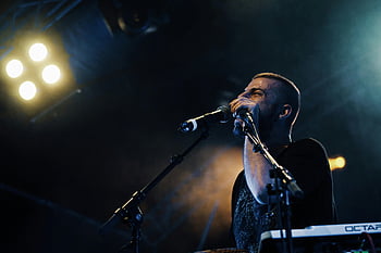 man holding microphone, performing on stage, live concert, male singer, band, bright stage lights, dynamic performance, microphone, stage, concert, singer
