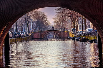 Amsterdam canal, bridge arch, city architecture, tranquil waters, canal view, brown bridge, vehicle-lined canal, urban scenery, canal bridge, cityscape, serene waterway