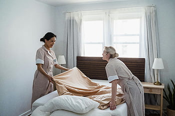 women putting bedsheets, housekeepers in uniform, making a bed, well-lit bedroom, efficient housekeeping service, bedroom scene, bed preparation, professional housekeeping, hotel room service, tidy bedroom, housekeeping duties