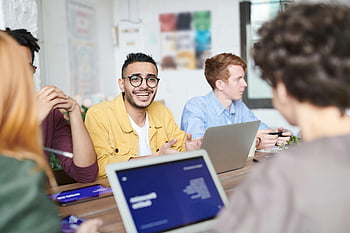 diverse group, discussing project, modern office, meeting room, yellow dress shirt, silver laptop, collaborative work, professional setting, team discussion, office environment, technology use