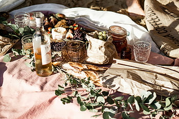 outdoor picnic, wine bottle, assorted snacks, rustic decor, labeled glass bottle, food, picturesque setting, picnic gathering, bread, cheese, eucalyptus leaves