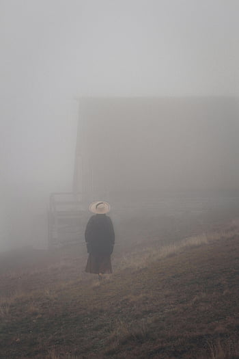osoba we mgle, samotna postać, kapelusz, mglisty teren wiejski, nastrojowa atmosfera, wiejski krajobraz, mglista pogoda, scena plenerowa, naturalne otoczenie, mgliste środowisko, widok na okolicę