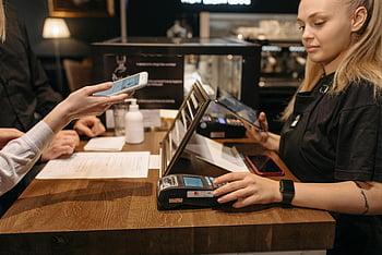 Kontaktloses Bezahlen, Café, Barista, Mobiltelefon, Zahlungsterminal, Kunde, Zähler, schwarzes Shirt, Coffee Shop -Theke, Barista bei der Arbeit, kontaktlose Transaktion