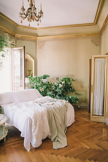letto bianco, Lussuosa camera da letto, arredamento chic, Accenti floreali, luce naturale, pavimento di legno, lampadario, Accenti d'oro, elegante interno, Camera da letto accogliente, biancheria da letto morbida