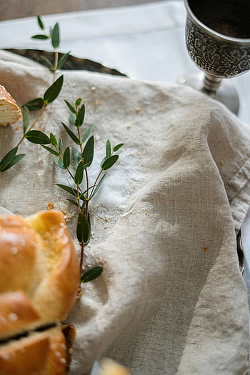 challah chléb, zeleň, stříbrný pohár, lněné tkaniny, detailní fotografie, tradiční jídlo, židovská tradice, Šabat, stálý život, teplé tóny, svislý výstřel