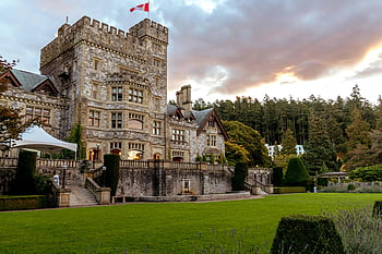 Hatley Castle, Victoria BC, stone castle, green grass, front yard, historic architecture, lush gardens, sunset view, Canadian flag, outdoor setting, scenic landscape