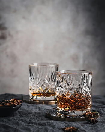 Křišťálové brýle whisky, Amber kapalina, texturovaný povrch, sofistikovanost, černý dřevěný stůl, čiré sklo, badyánu, skořice hole, Elegantní nápoj, rafinované nastavení, tmavé pozadí
