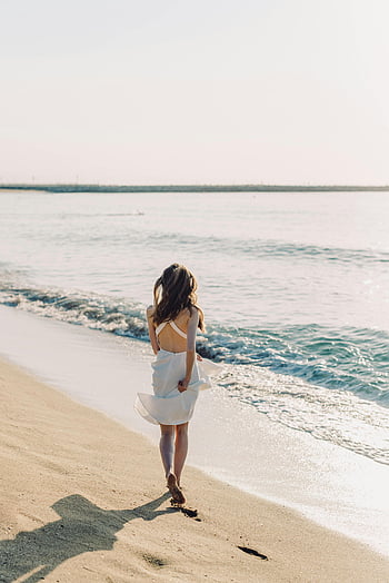 woman walking beach, white dress, tranquil beach, sunny skies, beach walk, ocean waves, sandy beach, beach scene, woman in dress, beach photography, coastal scene