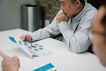 縞模様のシャツを着た男、 テーブルに座って、 読書紙、 実業家、 印刷ドキュメント、 事務机、 思慮深いレビュー、 プロの環境、 作業環境、 ドキュメント分析、 ビジネスミーティング