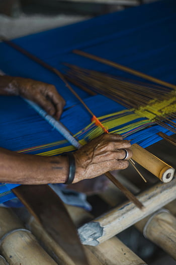 traditional loom, weaving, vibrant fabric, skilled craftsmanship, close-up hands, yellow and brown stick, textile art, cultural craft, handmade textiles, weaving process, artisan work
