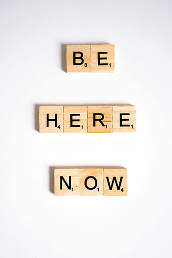 Scrabble tiles, Be Here Now, white background, close-up shot, inspiration, wooden tiles, motivational quote, minimalist design, word game, white surface, letter tiles