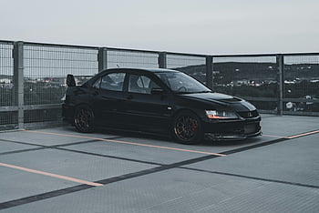 Black Mitsubishi Lancer Evolution, urban rooftop parking, dusk, stylish car, black car, Mitsubishi Lancer, rooftop parking lot, urban setting, car park, dusk lighting, stylish vehicle