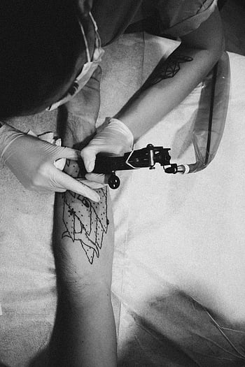 tattoo artist, tattoo machine, tattooing arm, unique pattern, monochrome, client arm, tattoo design, black and white, tattoo session, tattoo studio, tattoo process