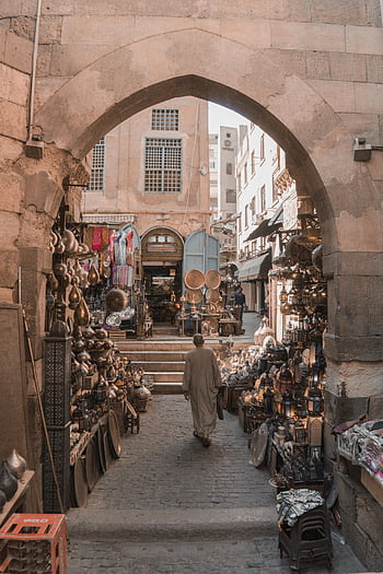 old town marketplace, man walking, artisanal stalls, charming entrance, warm atmosphere, old bazaar, cobblestone street, traditional market, historic architecture, cultural scene, vintage shops