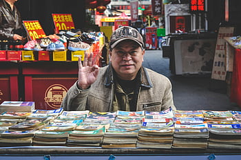 elderly vendor, brown coat, books, Tianjin street market, vibrant market, book selling, street vendor, outdoor market, cultural market, traditional market, book stall
