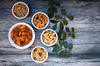 assorted nuts, white ceramic bowls, aerial view, rustic wooden table, green leaves, seeds, almonds, walnuts, cashews, granola, healthy snacks
