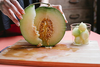 honeydew melon, cutting melon, healthy eating, indoor kitchen, fresh melon, melon preparation, melon seeds, wooden cutting board, glass bowl, melon slices, woman cutting melon