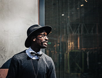 Man's Black Hat, fashion-forward man, eyewear, fedora, smiling, modern city backdrop, portrait, bow tie, stylish outfit, urban style, glasses