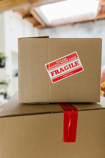 brown shipping boxes, fragile care label, cardboard boxes, indoor setting, close-up shot, stacked boxes, red tape, handle with care, thank you label, shipping package, delivery box