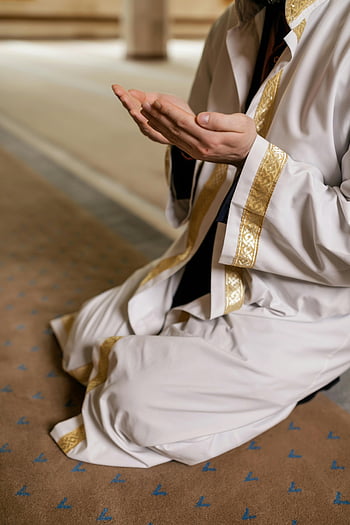 Muslim man, white thobe, kneeling prayer, mosque interior, Islamic clothing, prayer position, religious attire, traditional dress, spiritual practice, mosque setting, prayer gesture