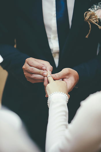 wedding ceremony, exchanging rings, elegant indoor, couple, close-up, man and woman, holding hands, wedding rings, formal attire, bride and groom, elegant wedding