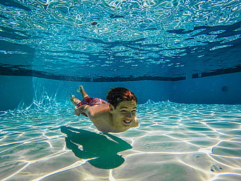 garoto sem camisa, natação debaixo d'água, iluminado, piscina, menino desfrutando, natação subaquática, chão da piscina, superfície da água, reflexos de luz, roupa de banho, fotografia subaquática