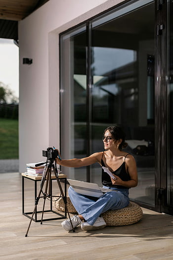 donna vlogging, canotta nera, jeans blu denim, pouf in vimini, vlogging interno, configurazione della fotocamera, il computer portatile, Abbigliamento casual, Home vlogging, tripode, luce naturale