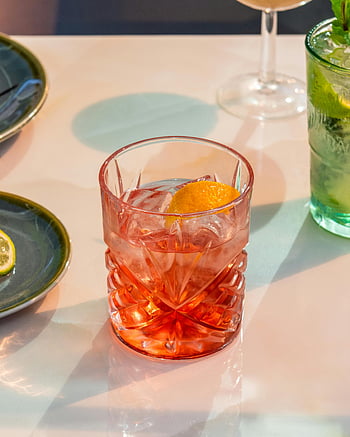 Negroni cocktail, classic Negroni, orange garnish, sunlit table, food presentation, drink presentation, glass of Negroni, cocktail glass, orange slice, table setting, refreshing drink
