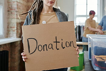 volunteer, donation sign, community center, clothing supplies, cardboard sign, charity event, volunteer work, donation drive, community service, non-profit organization, volunteer holding sign