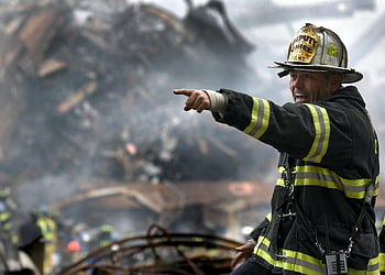firefighter, black and yellow uniform, pointing, disaster scene, rescue operations, smoke, debris, action, directing, safety gear, emergency response