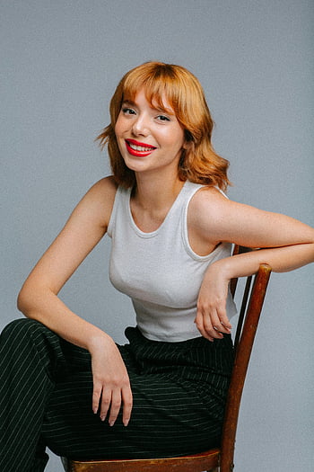 studio portrett, ung kvinne, Rødhåret kvinne, smilende kvinne, sitter på stolen, Studioinnstilling, hvit tank top, svarte pinstripebukser, rød leppestift, Uformell positur, profesjonell fotografering