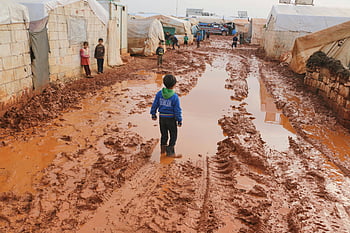 シリア難民キャンプ、 Idlib Syria、 泥だらけの道、 難民の子供たち、 汚れた地面、 ナビゲートする子供たち、 難民生活、 人道的危機、 変位、 キャンプ状態、 泥だらけの環境