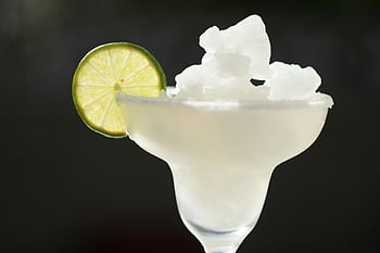 frozen margarita, lime garnish, summer refreshment, close-up drink, white ice, classic margarita, glass with lime, frozen cocktail, refreshing drink, white ceramic bowl, white ice cubes