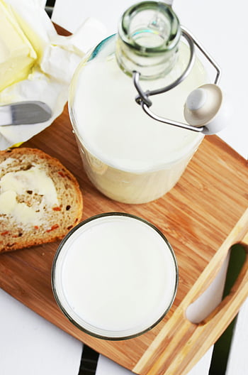 White Glass Bottle, milk bottle, buttered bread, wooden tray, rustic breakfast, high-angle view, glass of milk, breakfast scene, wooden surface, dairy products, fresh bread