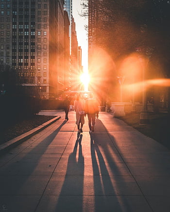 urban sunset, city street, long shadows, pedestrians walking, ray of sun, between buildings, captivating scene, urban landscape, sunset scene, city life, street photography