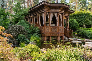 brown wooden gazebo, green trees, pond, lush greenery, tranquil pond, carved wooden gazebo, garden, outdoor, nature, peaceful setting, landscape