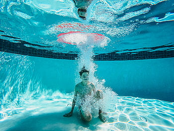 kid sitting under swimming pool, underwater playtime, clear swimming pool, boy enjoying water, surrounded by bubbles, underwater photography, pool bubbles, underwater fun, swimming pool activities, child underwater, pool play