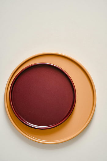 stacked plates, white surface, elegant composition, minimalist design, warm colors, round plates, terracotta plate, burgundy plate, modern tableware, flat lay, clean background