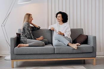 Ženy relaxační, moderní šedá pohovka, uvolněná konverzace, dvě ženy, neformální konverzace, pohodlné nastavení, Vnitřní nastavení, Útulná atmosféra, Přátelská interakce, Domácí prostředí, volný čas