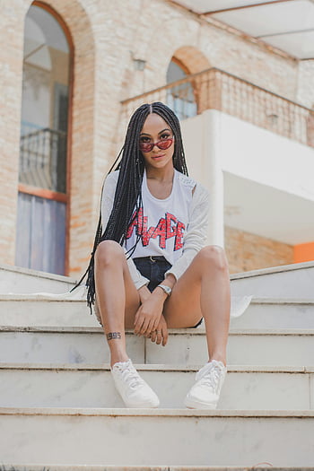 Donna seduta sulle scale, Giovane donna alla moda, scale urbane, occhiali da sole, trecce, posa sicura, scarpe da ginnastica bianche, Abbigliamento casual, sfondo di paesaggio urbano, architettura moderna, stile di strada