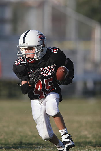 Boy Playing Football, Child athlete, American football, sunny day, determination, football player, youth sports, outdoor activity, sports uniform, football field, action shot