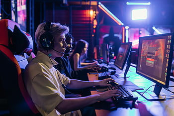 ゲーマー、 黒と銀のヘッドフォン、 競争力のあるゲーム、 没入型セットアップ、 ヘッドセット、 モニター、 ゲームセッション、 エスポート、 ゲーミングチェア、 ネオンライト、 マルチプレイヤーゲーム