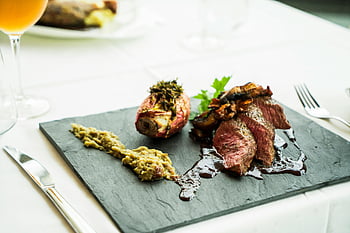 grilled meat, rectangular green board, steak, sauce, sides, wine, clean white table, plated steak, delicious meal, dining table, food presentation