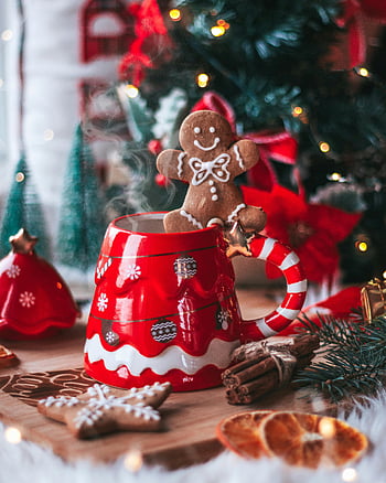 gingerbread man, hot drink, Christmas-themed mug, festive decor, cozy holiday scene, gingerbread cookie, Christmas tree, holiday season, cinnamon sticks, dried oranges, Christmas ornaments