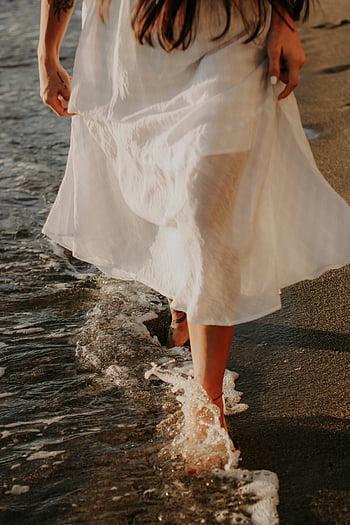 woman in white dress, walking barefoot, beach, touching waves, sea, sunset, coastal scene, barefoot woman, white dress, beach walk, waves crashing