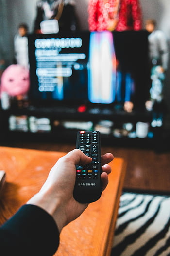 Samsung Remote Control, ruang keluarga, Malam film yang santai, orang yang memegang jarak jauh, Menonton tv, hiburan rumah, Suasana yang nyaman, penggunaan remote control, Pengaturan Hiburan, pengalaman menonton film, Remote TV Samsung
