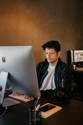 man in jacket, sitting, working, desktop computer, modern office, focused young man, eyeglasses, workspace, professional setting, computer work, office environment