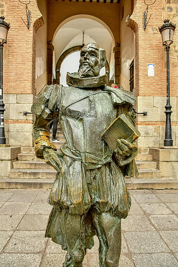 Statue of Miguel de Cervantes, historical figure, holding book, European architecture, bronze statue, literary monument, cultural landmark, outdoor sculpture, famous author, literary figure, public art