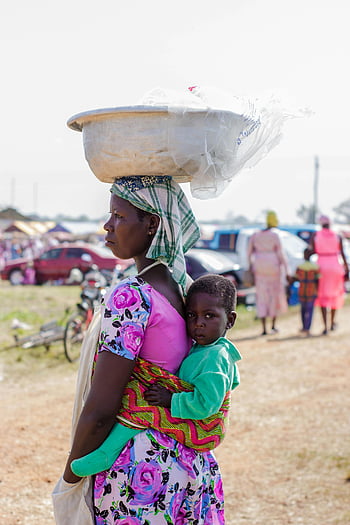 Black woman, child, basin on head, traditional sling, rural market, mother carrying child, lively market, African culture, outdoor scene, family life, daily activities