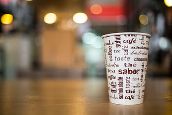 Kaffeetasse, Mehrsprachiger Text, Holztisch, lebendiges Café, Fotografie mit selektivem Fokus, weiße und braune Tasse, braune Holzoberfläche, Café -Einstellung, Mehrsprachige Wörter, Café, warmes Licht
